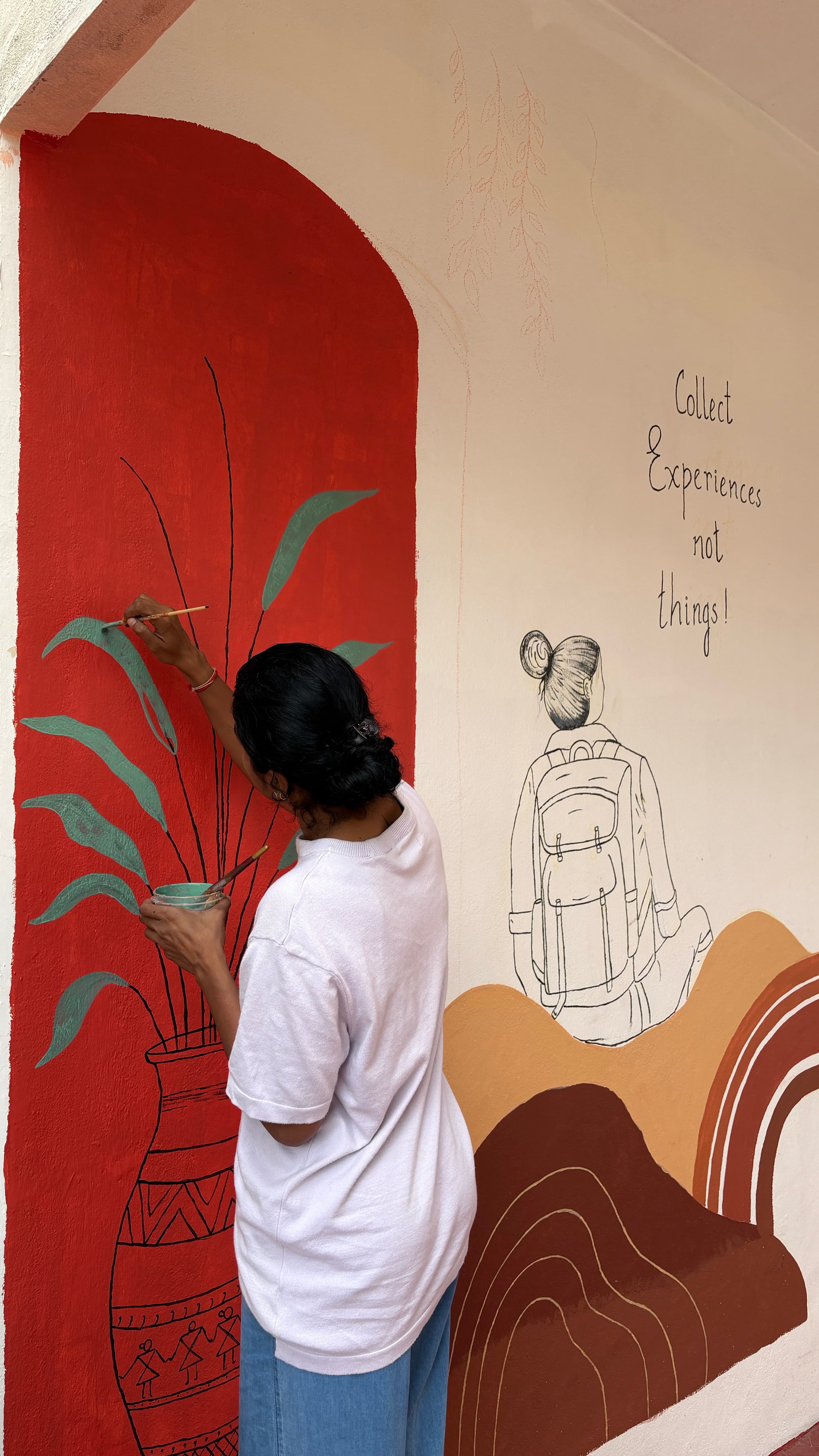 Artist painting the red arch mural with a plant motif